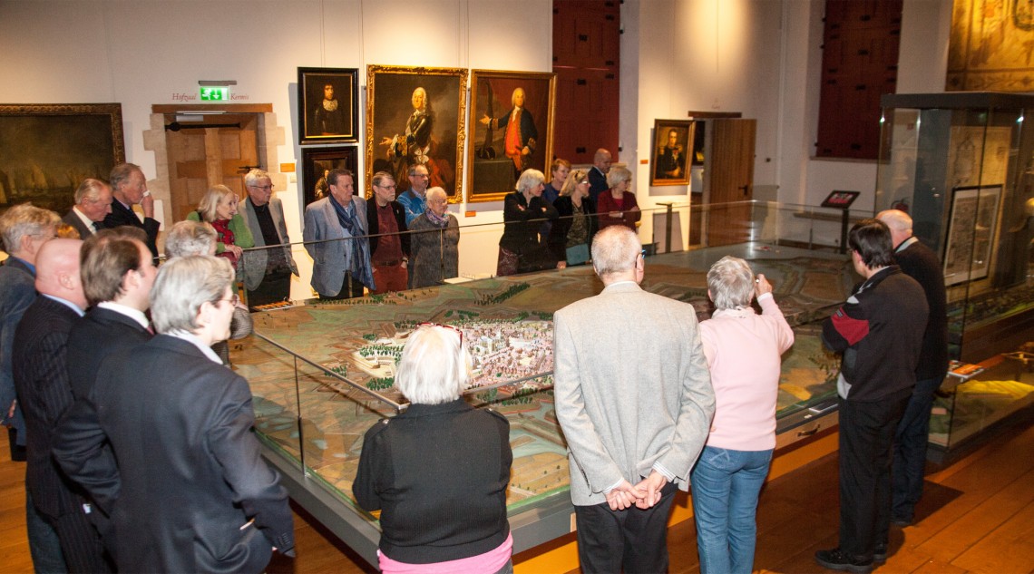 De nazaten van Carleton en Van Gorkum krijgen een toelichting op de aanval bij de maquette van Henk van Tilborg. Op de achtergrond kijkt J.E van Gorkum goedkeurend toe (links naast de deur).